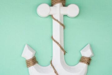White anchor wrapped in rope on a vibrant green background, symbolizing nautical themes.