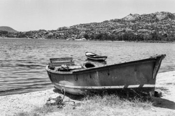 A vintage rowboat rests on the tranquil lake shore with distant mountains in Türkiye.