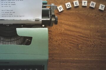 A typewriter creates poetic lines on paper amidst Scrabble tiles spelling 'POETRY'.